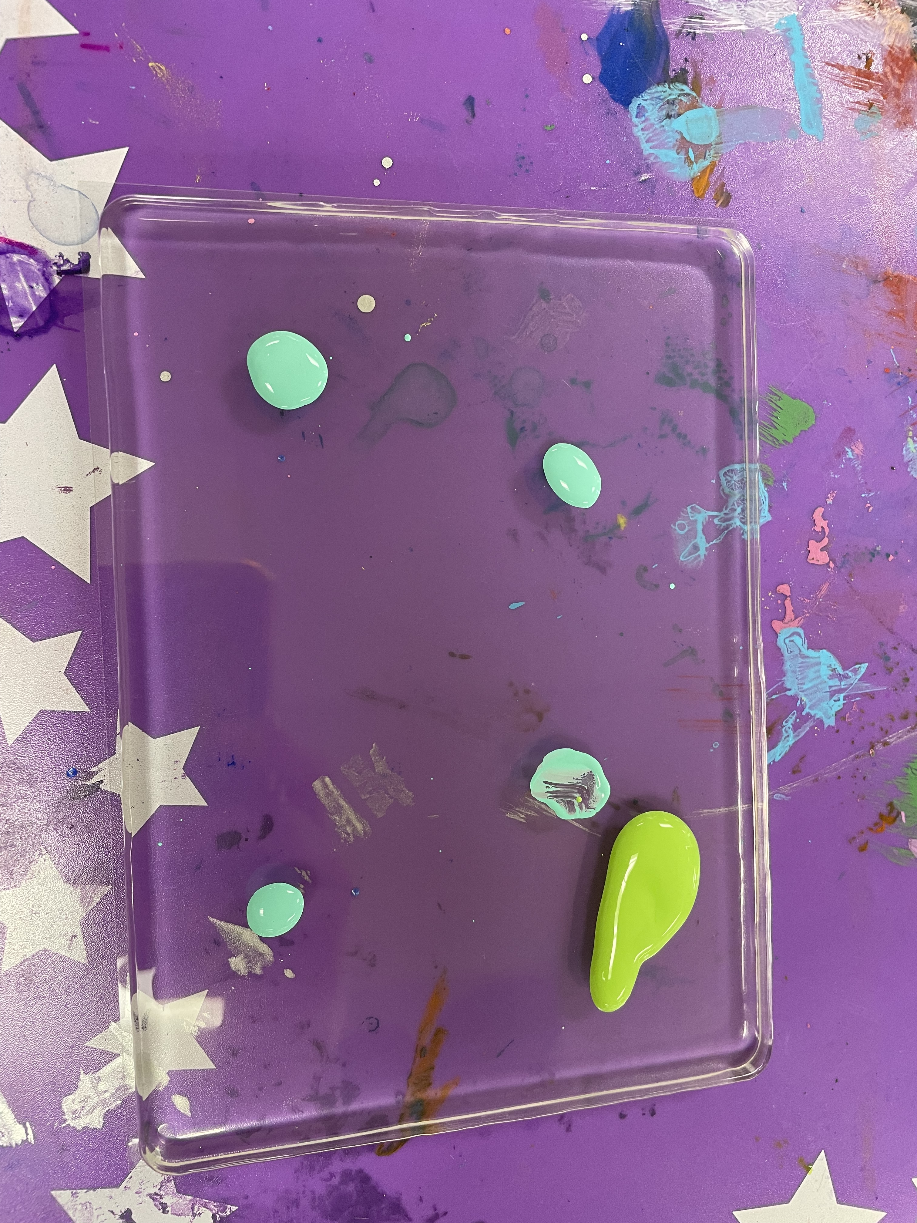A clear rectangular gel has five dollops of paint, four teal and one light green
