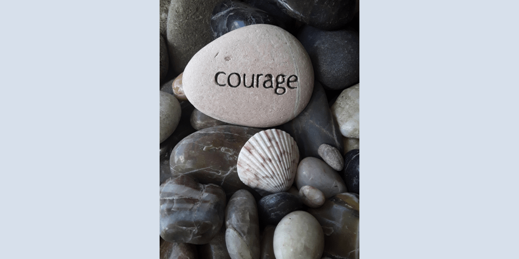 Courage is engraved on a rock set amidst smooth, weathered monochrome rocks