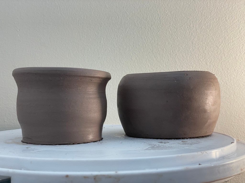 Two unfinished pots sit side-by-side. They're both a little lopsided but otherwise looking pretty even.